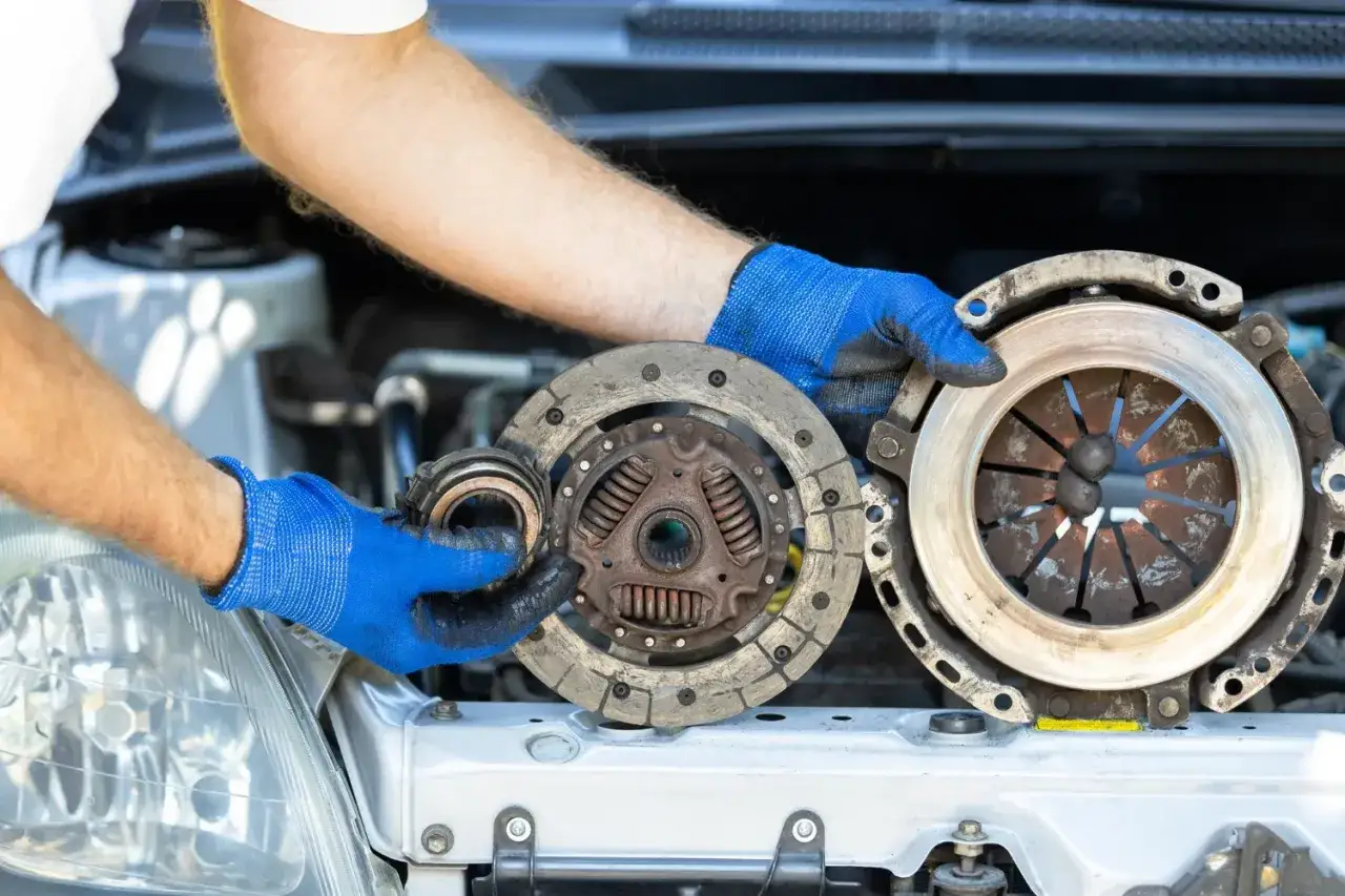 Mechanik w niebieskich rękawiczkach trzyma zużyte części sprzęgła. Zastanawiasz się, ile kosztuje wymiana sprzęgła?